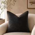 Black textured square pillow on a cream boucle armchair in a neutral living room.
