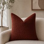 Rust red textured square pillow on a cream boucle armchair in a warm neutral room.