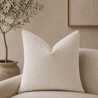 Cream textured square pillow on a boucle chair in a warm minimalist living room.