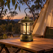 Army Green lantern lighting a camping table beside a tent at dusk.