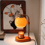 An elegant glass candle warmer lamp casting a soft orange glow, placed on a wooden base with a lit sandalwood and smoke candle.