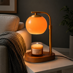 Elegant glass candle warmer lamp with a soft orange glow melting a jar candle on a white table next to a sofa.
