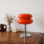 Glossy orange double-ring table lamp with chrome stem on a wooden surface.
