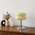 Glossy pale yellow mushroom table lamp with chrome base on a wooden console.