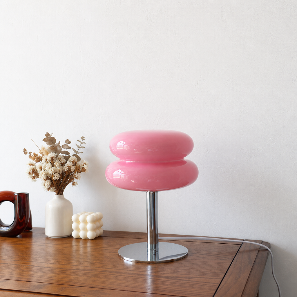 Glossy pink double-cushion lamp with chrome stem and round base on a wooden tabletop.
