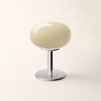 Glossy cream oval stool with a chrome pedestal and round base on a clean studio background.