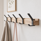 Light wood wall-mounted coat rack with black metal double hooks on a white wall.