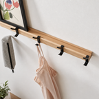 Wooden wall rail with black hooks holding a framed print, gray pouch, and pale pink camisole.