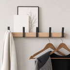 Wooden wall shelf coat rack with black hooks, framed prints, towel, and wooden hangers.