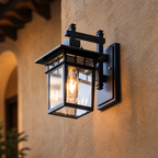 Black rectangular glass wall lantern with a glowing bulb mounted on a tan stucco wall.