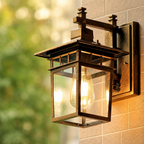 Bronze wall-mounted glass lantern with a glowing bulb on an outdoor brick wall.