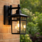 Black outdoor wall lantern with glowing bulb mounted on a tan brick wall.