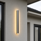 Vertical black outdoor wall light glowing warmly on a modern stucco exterior.