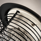 Close-up of a black wire fan grille over a cream metal motor housing.