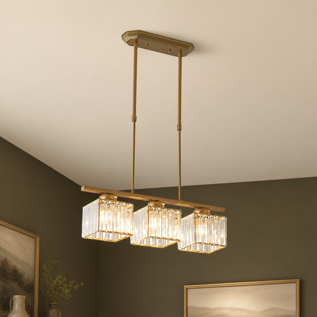 Gold three-light linear chandelier with cube crystal shades hanging from a ceiling.
