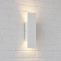 White rectangular wall sconce casting warm up and down light on a white brick wall.