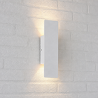 White rectangular wall sconce casting warm up and down light on a white brick wall.