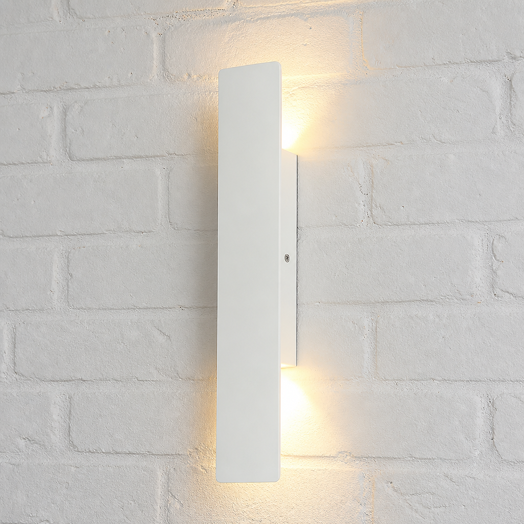 Slim white vertical wall light glowing warmly on a white brick wall.