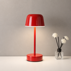 Glossy red dome table lamp on a white tabletop beside a small reed diffuser with white flowers.