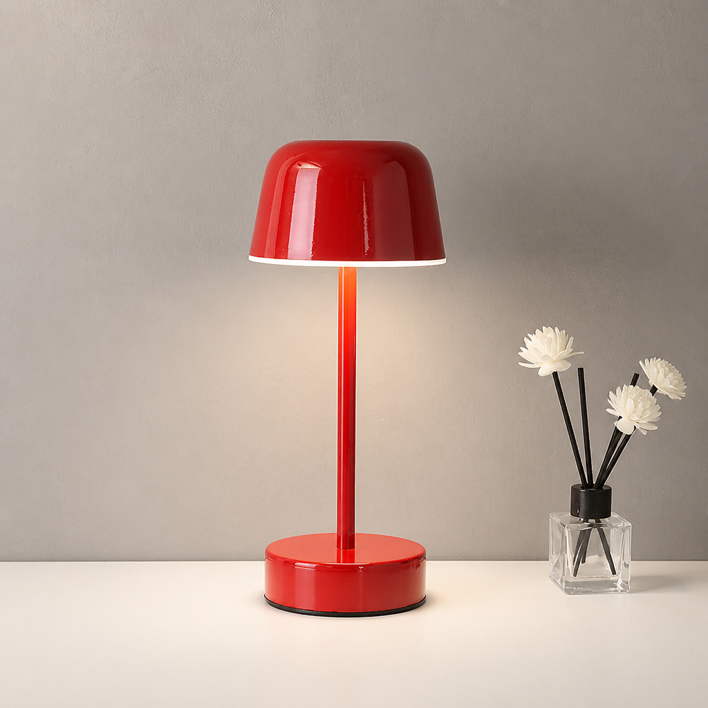 Glossy red dome table lamp on a white tabletop beside a small reed diffuser with white flowers.