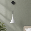 White cone wall pendant lamp with black mount and cord against a muted green wall.