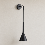 Black wall-mounted sconce with round backplate and tapered cone shade on a light wall.