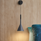 Dark gray cone wall pendant lamp glowing warmly beside teal cushions.