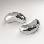 Two polished silver curved earbud-like devices on a clean light surface.