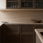 Dark wood kitchen cabinets with beige stone countertop and textured glass upper doors.