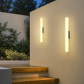 Two glowing vertical wall lights mounted on a cream outdoor wall beside wooden steps.