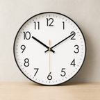 White round analog clock with black numerals, black rim, and gold second hand on a light wood surface.
