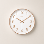 Round white wall clock with rose gold rim, numerals, and hands on a pale neutral background.