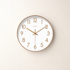 Round white wall clock with gold numerals and hands on a pale neutral background.
