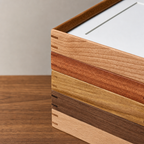 Stacked wooden tray corner showing five wood finishes on a wood tabletop.