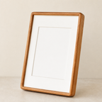 Wooden picture frame with white mat leaning on a neutral tabletop.