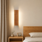 Vertical wooden wall sconce glowing above a bedside table and bed.