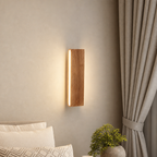 Wooden wall sconce with warm vertical light mounted beside a bed and curtains.