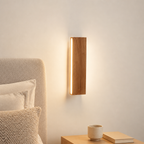 Wooden wall sconce with a warm vertical light beside a bed and nightstand.