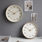 Two minimalist round analog clocks with cream faces and gold hands on a gray wall.