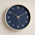 Navy blue round wall clock with cream rim and white numerals on a light wall.
