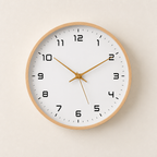 Round wood-rimmed wall clock with black numerals and gold hands on a pale wall.