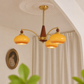 Three-arm chandelier with yellow glass shades and brass details hanging in a soft cream room.