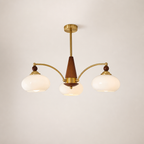 Three-light brass and wood chandelier with cream glass shades on a plain light background.