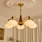 Brass and wood five-light chandelier with glowing cream glass shades mounted beneath a decorative ceiling medallion.