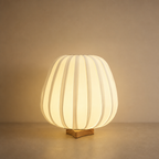 Glowing pleated cream table lamp with a small wooden base on a neutral surface.