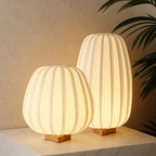 Two warm glowing ribbed table lamps with wooden bases sit on a light marble surface.