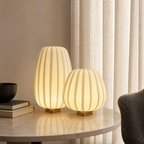 Two warm glowing ribbed table lamps with gold bases on a marble side table.