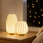 Two warm glowing ribbed fabric table lamps with small wooden bases on a bedside shelf.