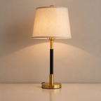Gold and black table lamp with a cream fabric shade glowing on a neutral tabletop.
