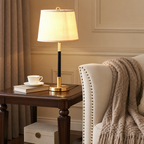 Brass table lamp with black stem and cream shade on a wooden side table beside an upholstered armchair.